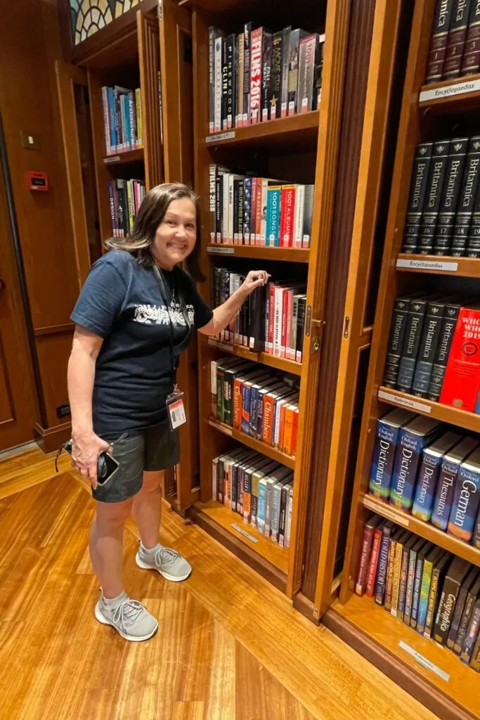 Woman standing in front of book case about to take a book from the cruise ship library.