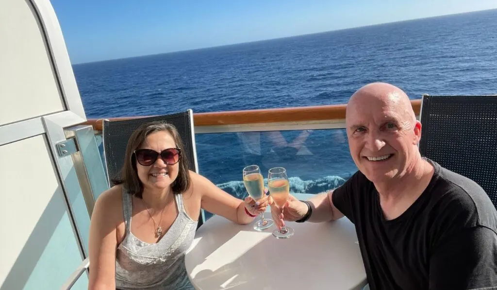 Couple toasting champagne while sitting on a cruise cabin balcony.